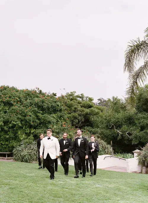 Group of men in suits walking on a grassy lawn outdoors with trees in the background