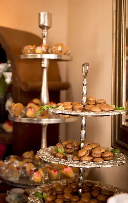 Tiered trays of assorted pastries and cookies on a dessert table in a warm indoor setting