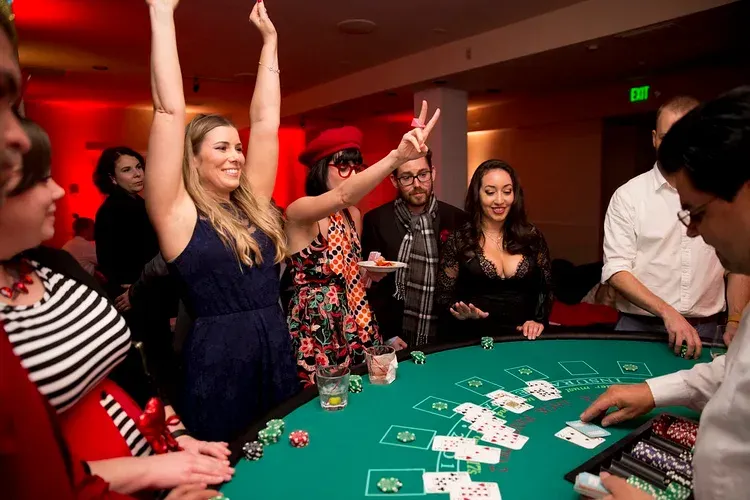 People cheering at a casino table as cards and chips are dealt on green felt