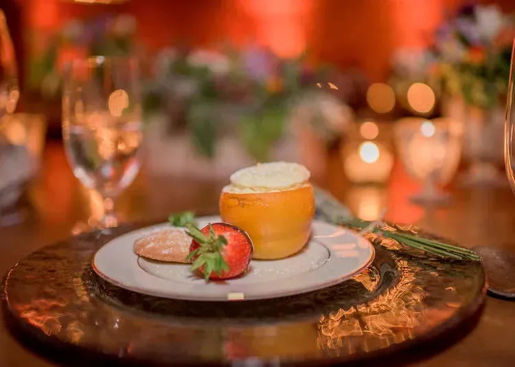 Dessert plate with a strawberry, cookie, and orange mousse on a copper tray at a candlelit table