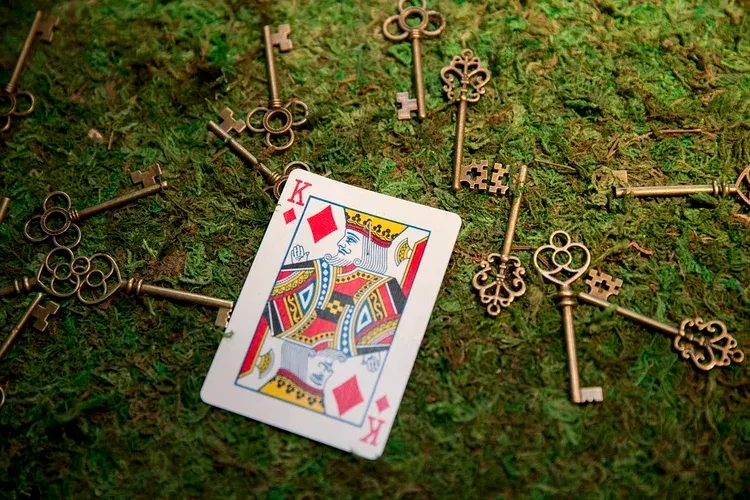 Queen of diamonds card lying on moss, surrounded by several vintage brass keys