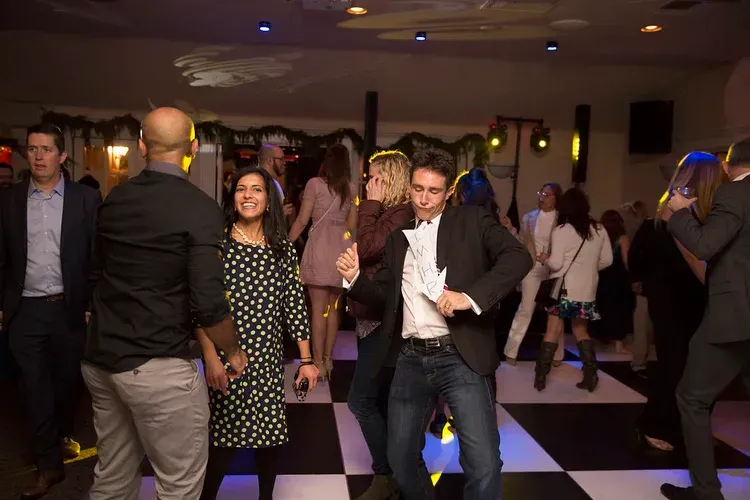 People dancing at a dimly lit indoor party with a checkered floor and colorful lights