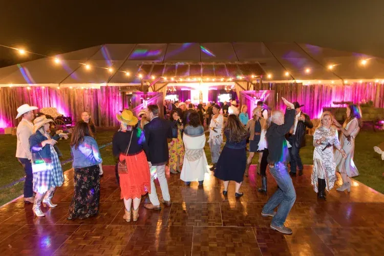 Guests dancing at a warmly lit indoor reception with string lights and pink drapery