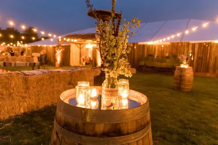 Lit outdoor reception with barrel table, candles, flowers, and string lights at dusk