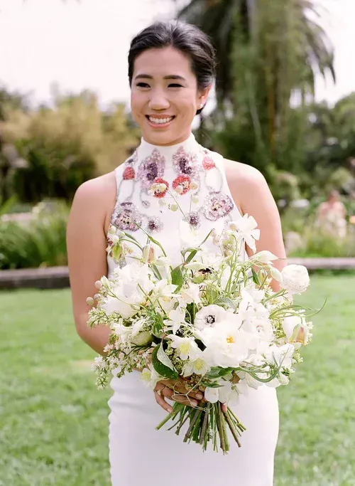 Woman in a white floral dress holding a bouquet of white flowers outdoors