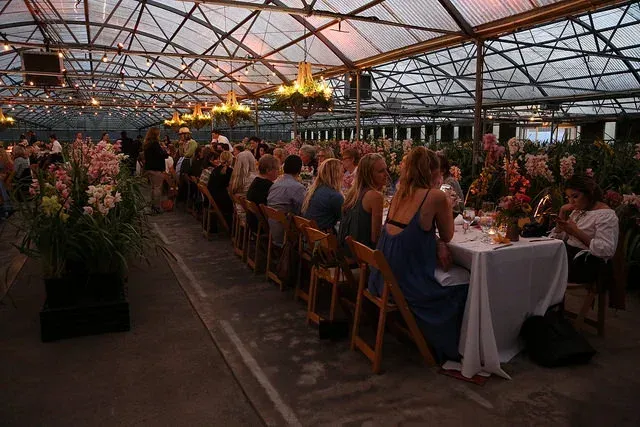 Long dining tables at a flower-filled event under a tent at dusk