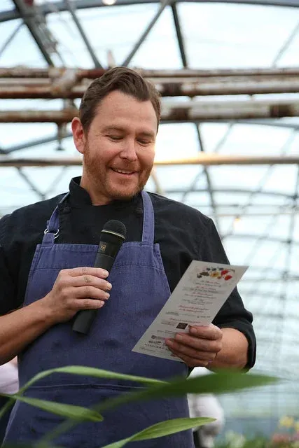 Man in an apron reading a menu card inside a greenhouse