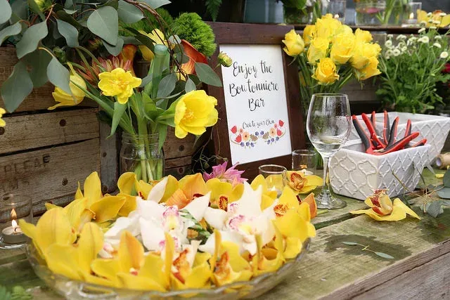 Yellow flowers and a sign on a rustic table with wine glasses and a bowl of red-striped straws