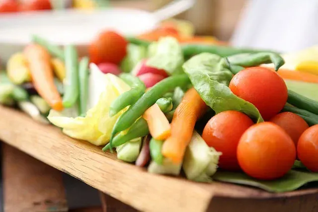 Fresh mixed vegetables on a wooden tray, including cherry tomatoes, green beans, carrots, and lettuce