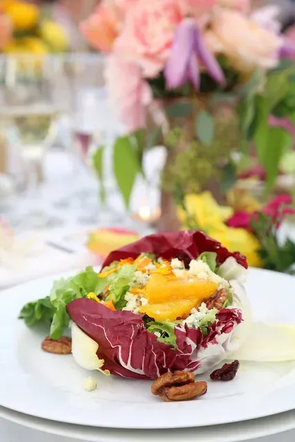 Gourmet salad with radicchio, greens, mango, and pecans on a white plate at a floral table setting