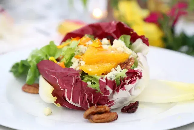 Colorful salad with red leaves, orange slices, greens, and nuts on a white plate