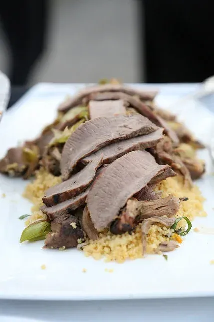 Sliced roast meat over couscous on a white plate