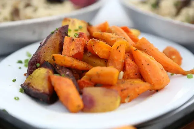 Roasted carrots and sweet potatoes on a white plate with herbs