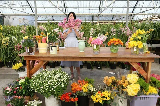 Woman arranging pink flowers at an outdoor market stall with colorful bouquets and potted plants