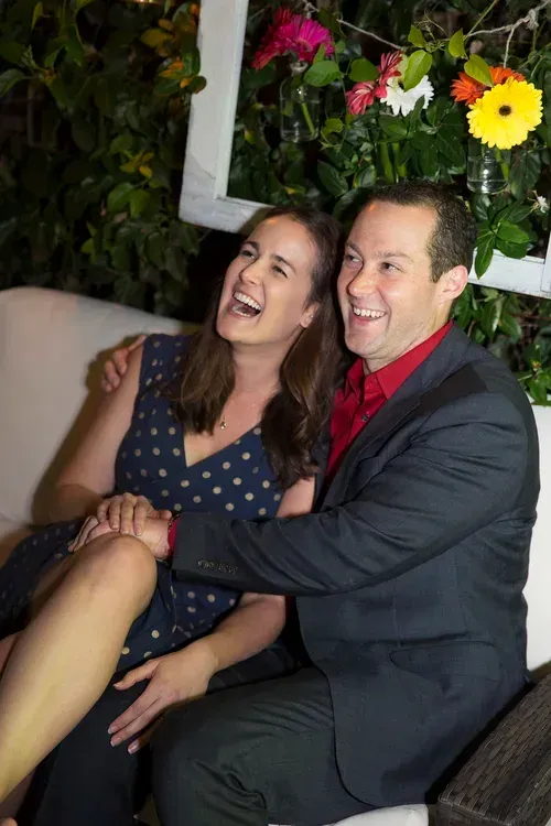 Smiling couple seated together at an indoor event with flowers and greenery in the background