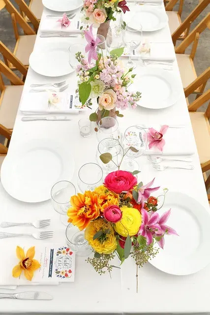 Elegant white dining table set with floral centerpieces in pink, yellow, and orange tones