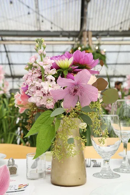 Pink and white floral centerpiece in a gold vase on a decorated table in a greenhouse