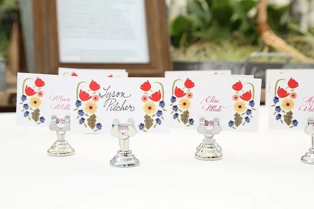 Floral place cards on silver stands with red, blue and yellow flowers at a white event table