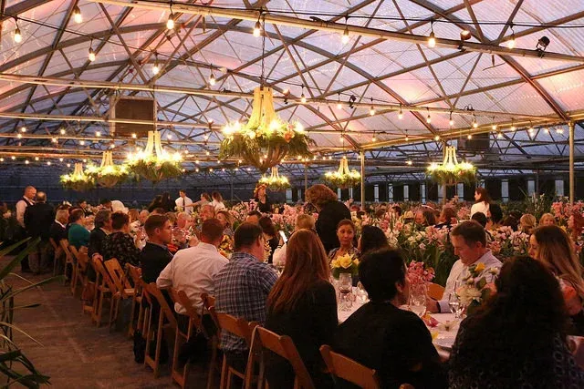 Large banquet under a lit transparent tent with chandeliers and long tables of seated guests