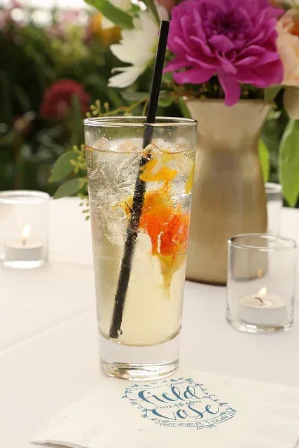 Tall citrus spritz with black straw on a white table, with flowers and candles in the background
