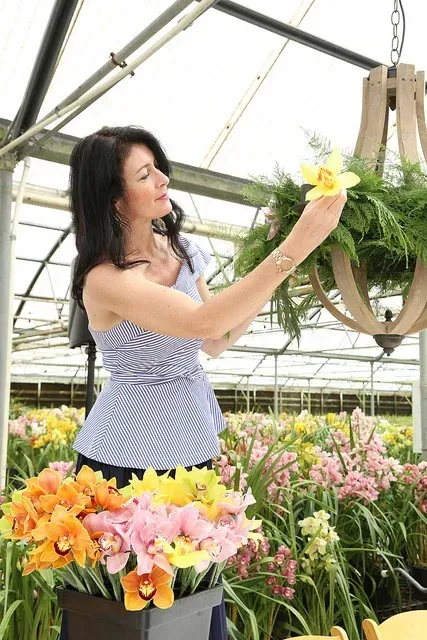 Woman in a greenhouse arranging yellow flowers beside blooming pink and orange plants