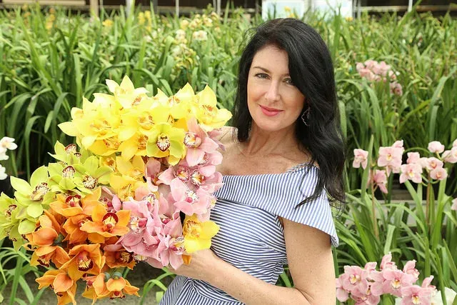 Woman holding a large bouquet of yellow, pink, and orange flowers in a garden setting