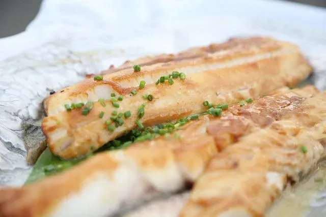 Grilled fish fillets topped with chopped herbs on a white plate