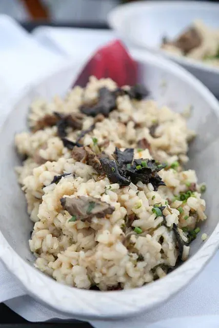 Bowl of rice topped with mushrooms and herbs, served with a red garnish