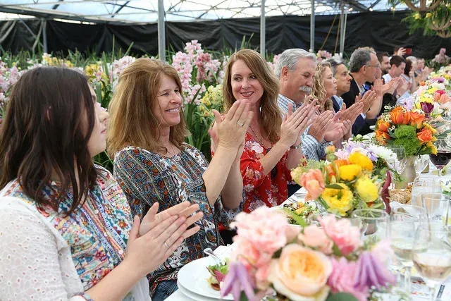 Guests applauding at a decorated outdoor banquet table with colorful flowers and plates of food