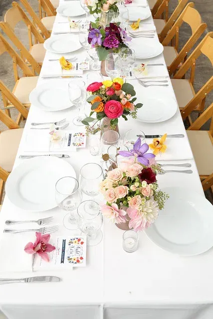 Long banquet table set with white dishes, gold chairs, and colorful floral centerpieces