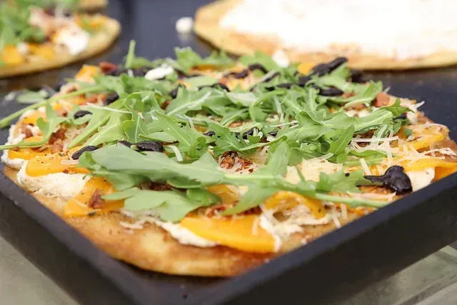 Close-up of a pizza topped with arugula and melted cheese on a dark baking tray