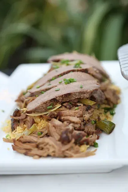 Sliced roast meat over rice on a white plate, garnished with chopped herbs