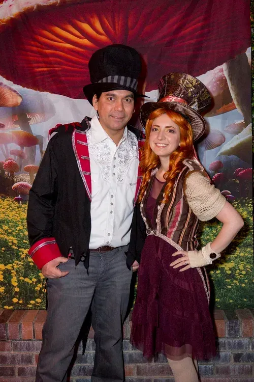 Two people in festive costumes posing in front of a colorful backdrop.