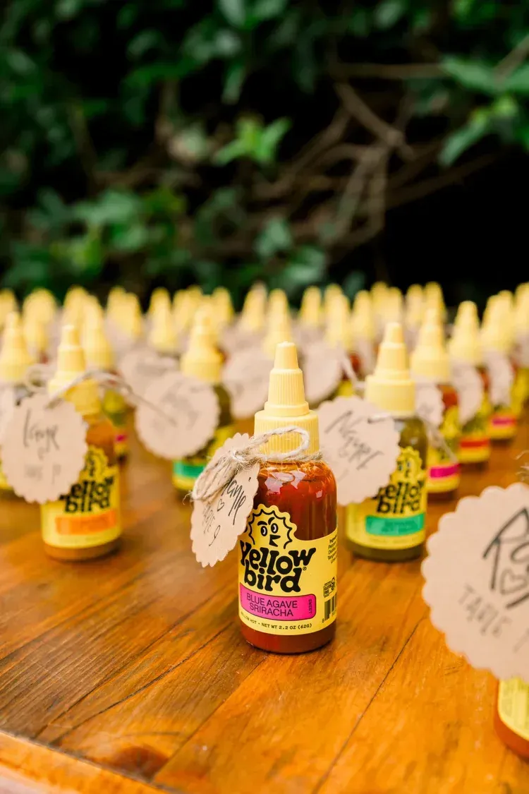 Rows of small bottled drinks with yellow caps on a wooden table, labels facing forward outdoors.