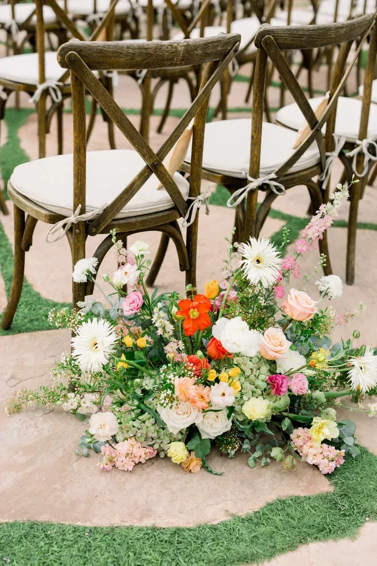 Floral arrangement with white, pink, and orange flowers beside wooden chairs on a patio