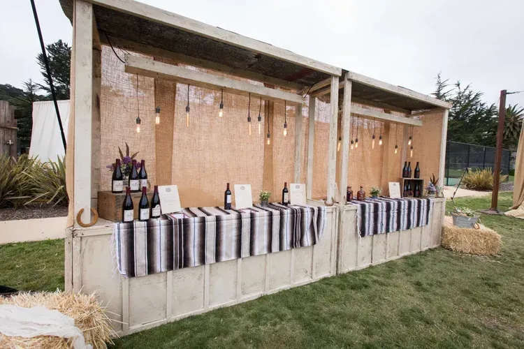 Outdoor market stall with bottles and goods displayed on a striped tablecloth under a simple wooden canopy
