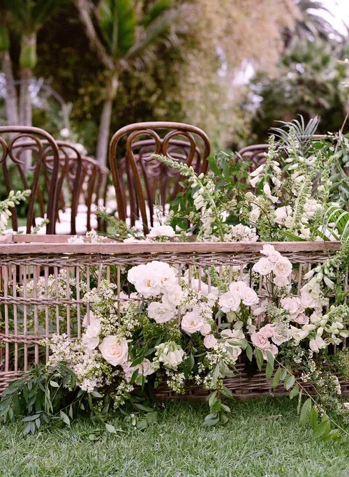 Rustic garden chairs and a bench decorated with pale pink and white flowers on green grass