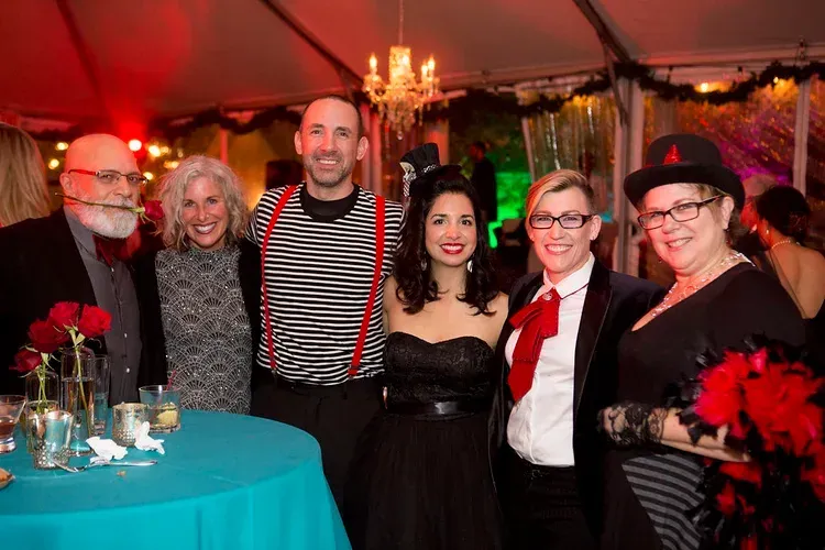 Six people posing at a festive event with red lighting and a teal table in the foreground