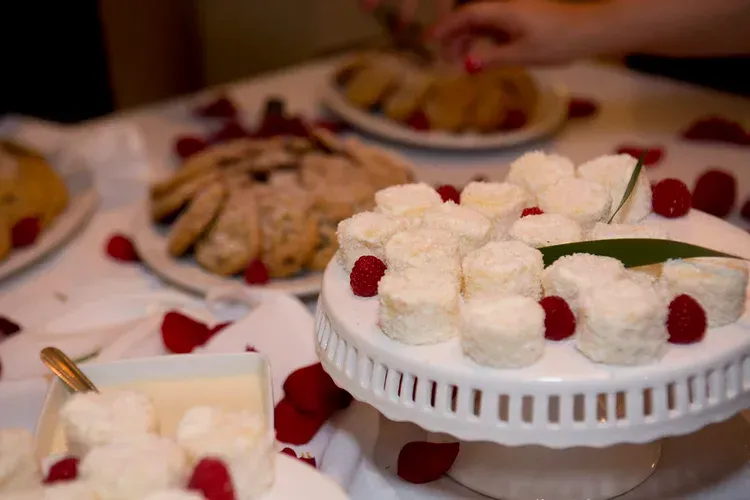 Dessert table with white-frosted pastries on a stand and plates of sweets with red berries.