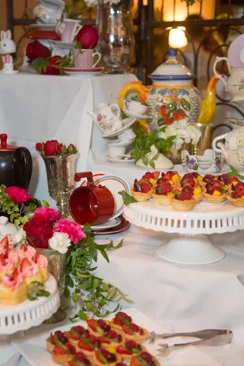 Dessert buffet table with pastries, fruit tarts, tea set, and floral decorations