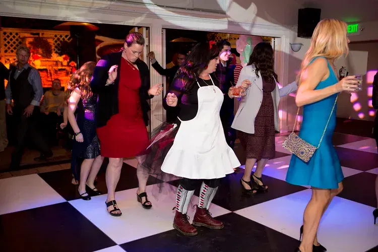 People dancing at a lively party on a black-and-white checkered floor under colorful lights
