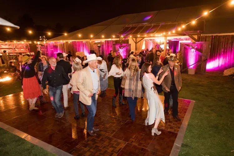 Guests dancing at an outdoor evening party under pink and warm string lights in a tented venue
