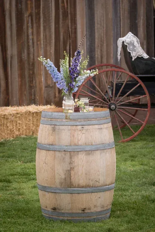 Wooden barrel with wildflowers in front of a barn and wagon wheel