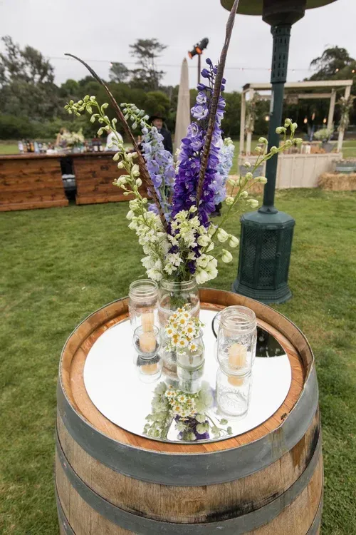 Floral centerpiece in glass vases atop a wooden barrel table at an outdoor garden event
