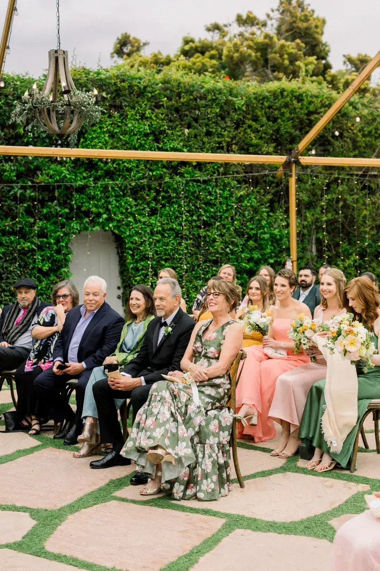Guests seated outdoors at a garden wedding ceremony, with floral chairs and bamboo decor