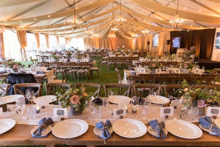 Elegant banquet tent with long rows of set tables, white drapes, warm string lights, and floral centerpieces