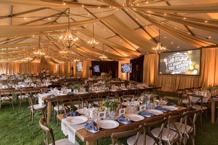 Elegant banquet tent with long wooden tables, string lights, and a grassy floor set for an event