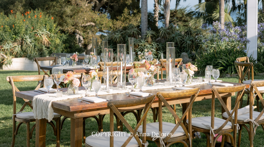 Elegant outdoor dining table set with white decor and flowers in a garden setting