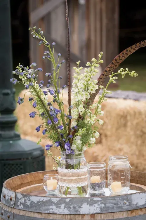 Wildflowers in a glass vase on a rustic table with candles and a hay bale backdrop