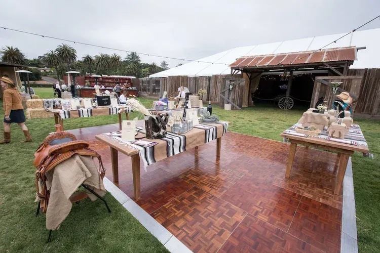 Outdoor craft fair with tables of handmade goods on a wet brick path under white tents